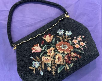 May include: A vintage black beaded handbag with a curved handle and gold trim. The bag features an embroidered floral design in shades of pink, orange, and blue. The handle is also beaded.