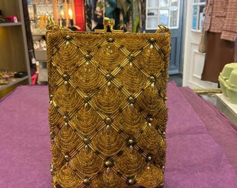 May include: A rectangular gold beaded clutch bag featuring a repeating fan-shaped pattern arranged in a diamond grid. The bag has a metallic gold frame with a top clasp closure and a delicate gold chain strap attached to the upper corners.