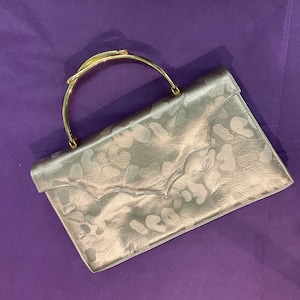 May include: A silver clutch purse with a gold-toned handle. The purse has a textured, animal print design.