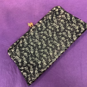 May include: A black fabric clutch purse with a gold clasp and a floral pattern.