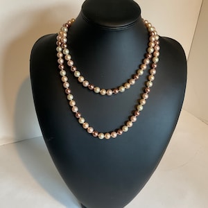 May include: A long, double-strand pearl necklace with alternating light and dark pink pearls.