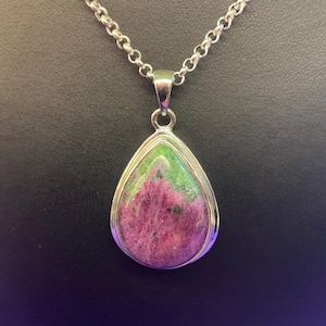 May include: A silver pendant necklace with a teardrop-shaped gemstone. The stone displays pink and green colours, set in a silver bezel. The chain is a delicate silver link design, suitable for everyday wear.