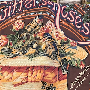 May include: A decorative scarf featuring a detailed illustration of birds, roses, and a straw hat. The color palette includes shades of brown, orange, and red, with the text "Witters & Roses" and "Daniel Hechter - Paris" visible.