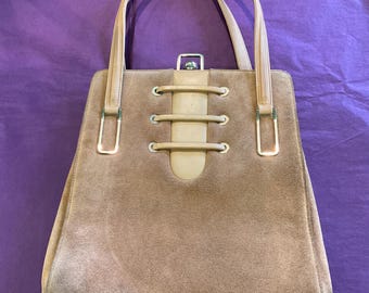 May include: A brown suede handbag with a beige leather flap and a silver clasp. The bag has a top handle and a lace-up detail on the front.