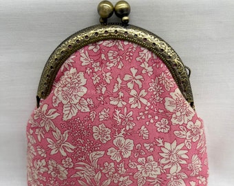 May include: A pink fabric coin purse with a floral pattern and a brass clasp.