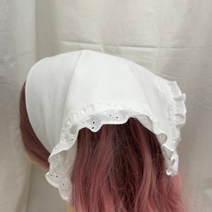 Puede incluir: Bandana de algod&oacute;n blanco con ribete de encaje blanco. La bandana est&aacute; doblada y atada alrededor de la cabeza de un maniqu&iacute;.