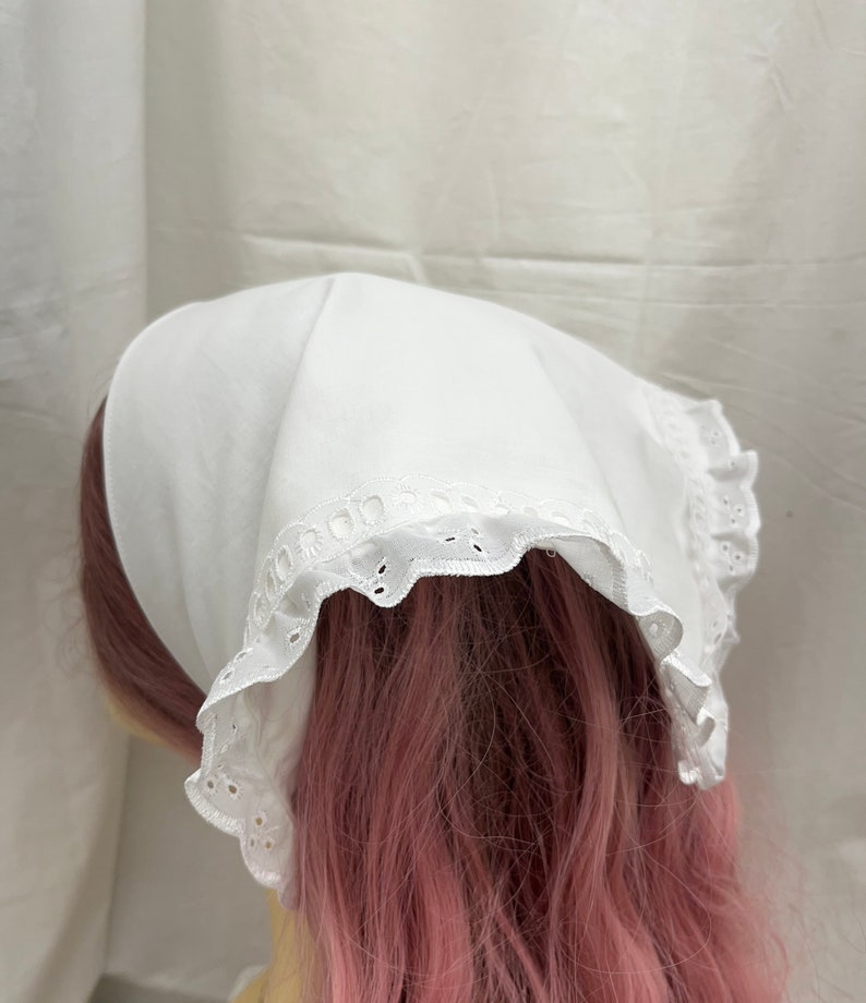 Puede incluir: Bandana de algod&oacute;n blanco con ribete de encaje blanco. La bandana est&aacute; doblada y atada alrededor de la cabeza de un maniqu&iacute;.