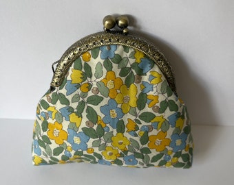 May include: A small, floral patterned coin purse with a brass clasp. The fabric is white with yellow and blue flowers.