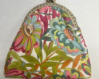 May include: A small, cream-colored coin purse with a floral pattern in shades of pink, green, and orange. The purse has a gold-toned metal frame with a clasp.