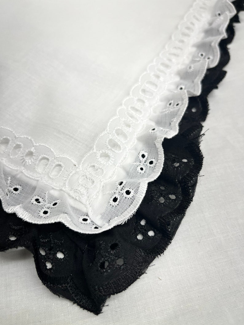 Puede incluir: Dos capas de encaje blanco y negro con bordes festoneados. El encaje tiene un delicado patr&oacute;n de ojales.