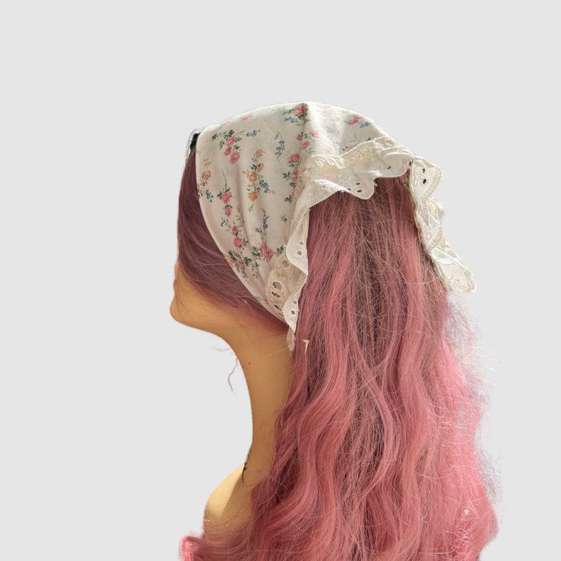 May include: A white floral print bandana with lace trim tied around a pink wig.