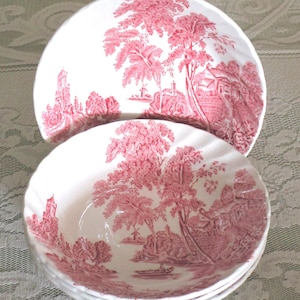 May include: A stack of white ceramic bowls and a plate with a red toile pattern. The pattern depicts a landscape with trees, buildings, and a windmill. The bowls have a scalloped edge.