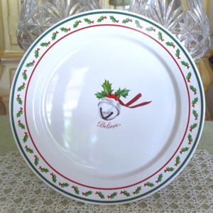 May include: White ceramic Christmas plate with a green and red holly berry border. The plate features a bell with holly and the word "Believe".
