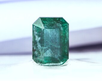 May include: A deep green emerald gemstone with a faceted cut. The emerald is set on a white background.