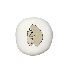 May include: A white round pillow with a simple line drawing of two brown bears hugging each other.