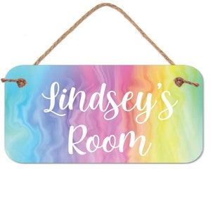 May include: A rainbow-colored wooden sign with the text "Lindsey's Room" in white lettering. The sign has a rope hanger.