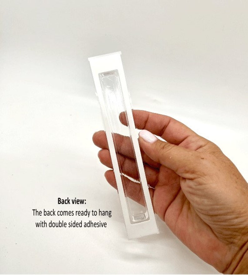 May include: White plastic frame with a clear plastic insert. The back of the frame has double-sided adhesive for hanging. Back view: The back comes ready to hang with double sided adhesive.