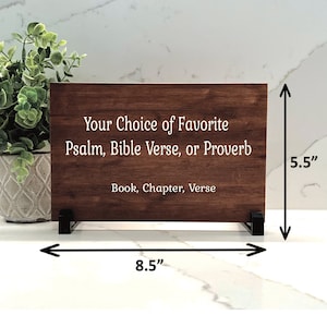 Pode incluir: Uma placa de madeira com uma mancha marrom, medindo 8,5 polegadas de largura e 5,5 polegadas de altura, com o texto "Your Choice of Favorite Psalm, Bible Verse, or Proverb Book, Chapter, Verse" em letras brancas.