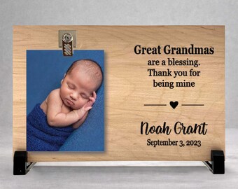 May include: A rectangular light-colored wooden plaque featuring a metal clip holding a photograph of a newborn baby wrapped in a blue blanket. The wood is engraved with the text: Great Grandmas are a blessing. Thank you for being mine, Noah Grant, September 3, 2023.