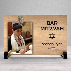 May include: A wooden Bar Mitzvah photo frame with a picture of a young person wearing a yarmulke and tallit. The frame has the words "BAR MITZVAH", a Star of David, the name "Zachary Ryan", and the date "6.22.23" printed on it.