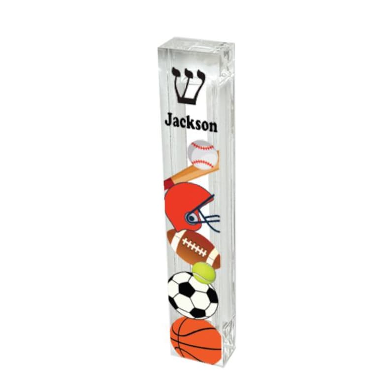 May include: A clear acrylic sports themed personalized bar mitzvah or bat mitzvah  candle holder with the name "Jackson" and a Star of David. The holder features a baseball, football, basketball, soccer ball, and a baseball bat.