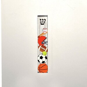 May include: A clear acrylic mezuzah with a sports theme. The mezuzah features a baseball, football, basketball, soccer ball, and a baseball bat. The mezuzah is decorated with a Hebrew letter Shin.