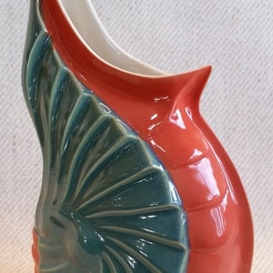 May include: A ceramic vase with a unique design. The vase features a vibrant color scheme, with a coral-red body and a teal-colored, fan-shaped accent. The interior is white. The vase has a curved, organic shape, adding to its artistic appeal.