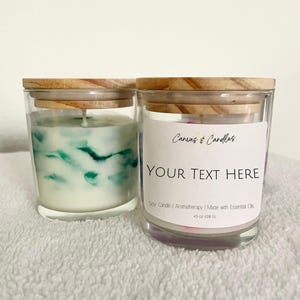 Op de afbeelding: Twee glazen potkaarsen met houten deksels. Eén kaars heeft een wit en groen wervelontwerp, de andere heeft een label met de tekst "Canvas & Candles" en "YOUR TEXT HERE". De kaarsen zijn 128 gram en gemaakt met essentiële oliën.