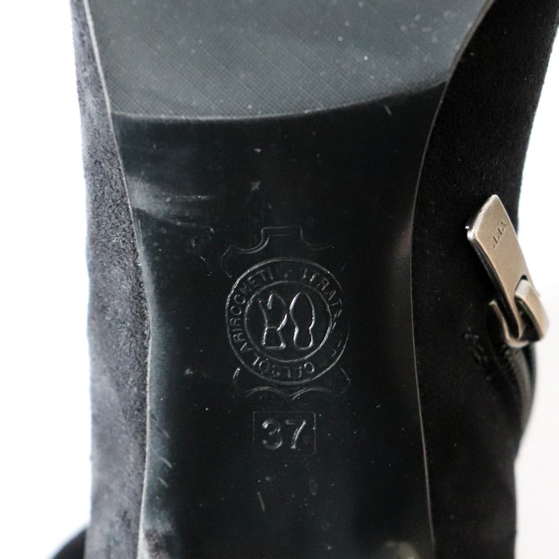 May include: Close-up of a black suede boot with a zipper and a leather sole. The sole features a circular emblem with the number 20 and the size 37.