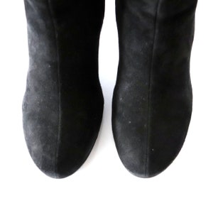 May include: A pair of black suede boots, viewed from the toe up. The boots have a soft, matte texture and a classic design. The image is set against a clean white background.
