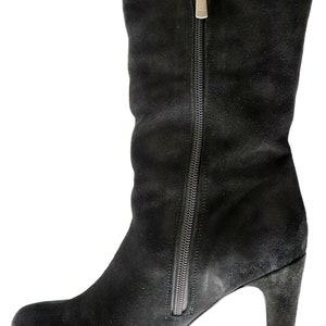 May include: Black suede knee-high boot with a side zipper and a high heel. The boot has a rounded toe and a silver zipper pull. The suede material has a slightly worn appearance.