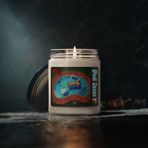 May include: A lit candle in a glass jar with a black lid. The label features a pool scene with a person on a float, a beach ball, and the text "Pool Jesus". The candle sits on a dark, reflective surface.