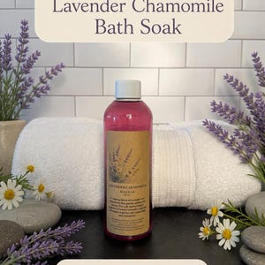 May include: A clear plastic bottle filled with purple liquid labeled Lavender Chamomile Bath Soak 8 oz. The bottle features a tan label with a lavender and chamomile illustration. The text reads Lavender Chamomile Bath Soak 8 oz.
