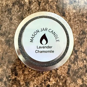 May include: A silver mason jar candle lid with a white label that reads "Mason Jar Candle" with a flame icon and the text "Lavender Chamomile".