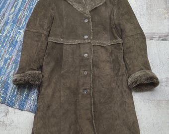 May include: A long, dark olive-brown coat featuring a soft, fuzzy faux-fur lining and trim along the collar, cuffs, and front opening. The coat has a button-down front closure with five visible dark buttons and a structured, knee-length silhouette.