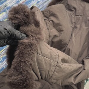 May include: A brown quilted jacket with a fur-trimmed hood and cuffs. The jacket is a solid color and appears to be made of a soft, padded material. The fur trim is a darker shade of brown.