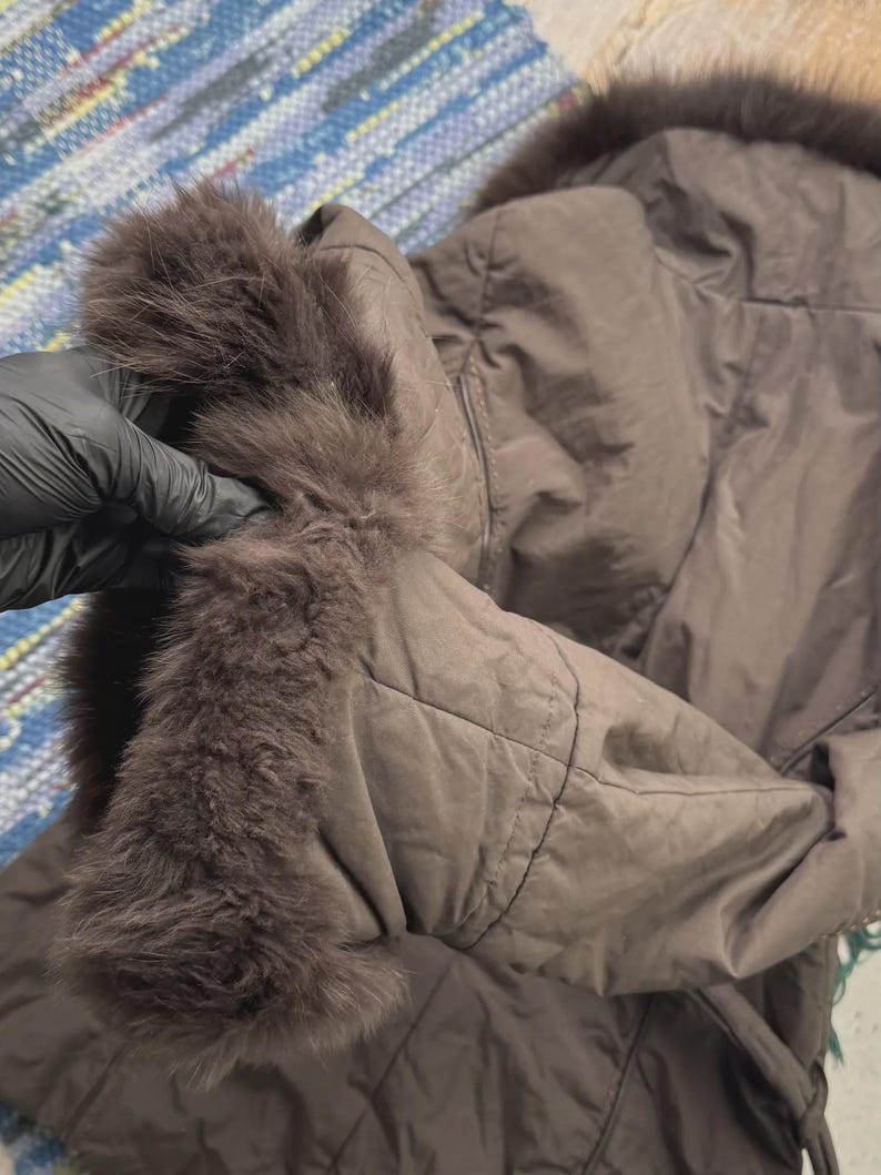 May include: A brown quilted jacket with a fur-trimmed hood and cuffs. The jacket is a solid color and appears to be made of a soft, padded material. The fur trim is a darker shade of brown.