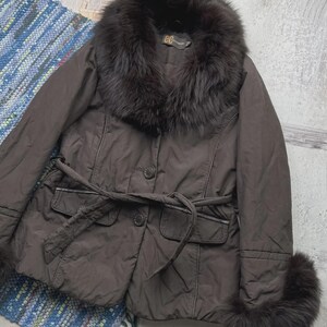 May include: A brown jacket with a fur collar and cuffs. The jacket has a belted waist, two front pockets, and button closures. The fur appears to be dark brown. The jacket is a stylish outerwear piece.