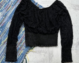 Può includere: Top nero in pizzo a maniche lunghe con vita e polsini arricciati. Il top ha uno scollo tondo ed è realizzato in delicato pizzo trasparente. Le maniche sono lunghe e aderenti, e la vita è stretta con una fascia arricciata.