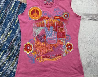 May include: Pink sleeveless shirt with a graphic print of a peace sign, the text "The Fantasy", and the text "Avalon Solarium".
