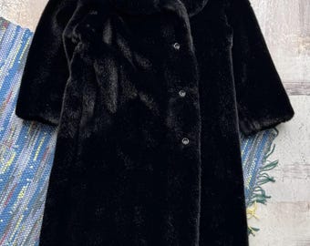 May include: A long-sleeved black faux fur coat featuring a wide collar and a front button closure with three visible dark buttons. The coat has a straight silhouette and a plush, textured surface throughout the entire garment.