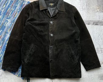 May include: A black suede jacket with a button closure and a collared neckline. The jacket has two pockets on the front and a label on the left side of the chest that reads "El Charro".