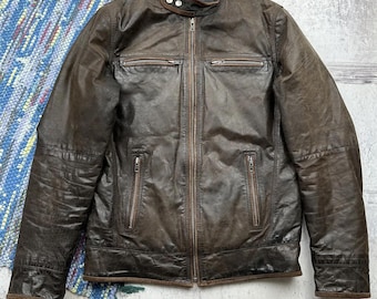 Puede incluir: Una chaqueta de cuero marrón para moto con cierre de cremallera y varios bolsillos.