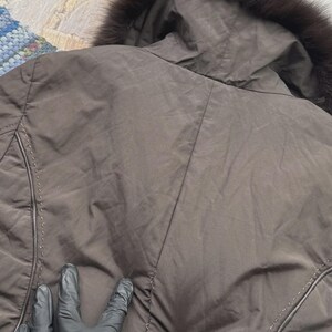May include: A brown jacket with a hood trimmed with dark fur. The jacket has a quilted design and visible stitching details. The image shows the back of the jacket.