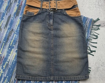 Puede incluir: Falda vaquera con cinturón y bolsillos de pana marrón. La falda tiene un lavado azul descolorido y una hebilla metálica en el cinturón. La falda se muestra sobre una alfombra estampada azul y blanca.