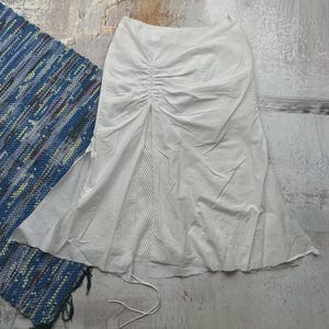 May include: A white skirt with a mesh panel and a drawstring waist. The skirt has a side slit and a relaxed fit.