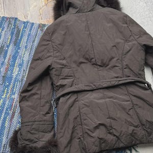 May include: A brown winter coat with a fur-lined hood and cuffs. The coat has a belt at the waist and a quilted design. The coat is made of a smooth, shiny material and appears to be in good condition.