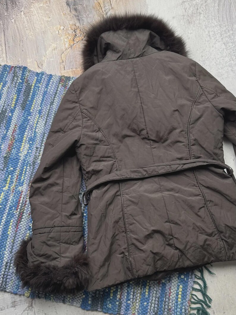 May include: A brown winter coat with a fur-lined hood and cuffs. The coat has a belt at the waist and a quilted design. The coat is made of a smooth, shiny material and appears to be in good condition.