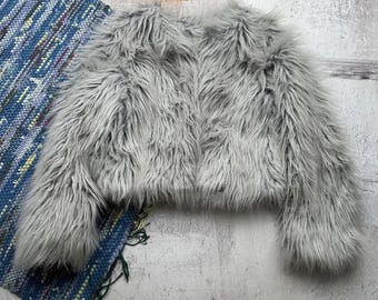 May include: A gray faux fur jacket with long sleeves and a cropped length.