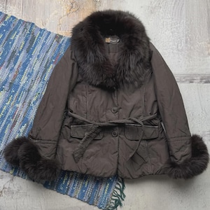 May include: A brown jacket with a fur collar and cuffs. The jacket has a belted waist and button closure. The fur is dark brown, and the jacket appears to be made of a quilted material. The jacket is displayed on a blue and white rug.